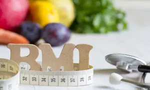 Litery "BMI" owinięte miarką, obok stetoskop i owoce. Zdjęcie sugeruje, czym obniżyć ciśnienie bez leków: zdrową dietą i kontrolą wagi.