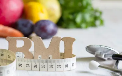 Litery "BMI" owinięte miarką, obok stetoskop i owoce. Zdjęcie sugeruje, czym obniżyć ciśnienie bez leków: zdrową dietą i kontrolą wagi.