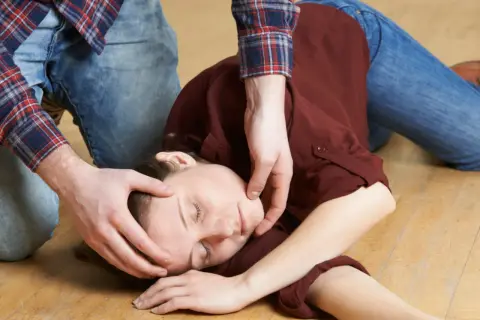 Osoba w pozycji bocznej bezpiecznej, z ręką pod głową, na podłodze.