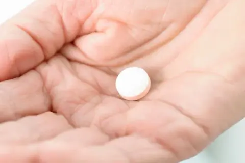 Dłoń trzyma białą tabletkę. Czy paracetamol podnosi ciśnienie? To pytanie nurtuje wiele osób.