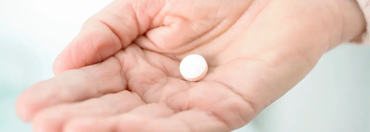 Dłoń trzyma białą tabletkę. Czy paracetamol podnosi ciśnienie? To pytanie nurtuje wiele osób.