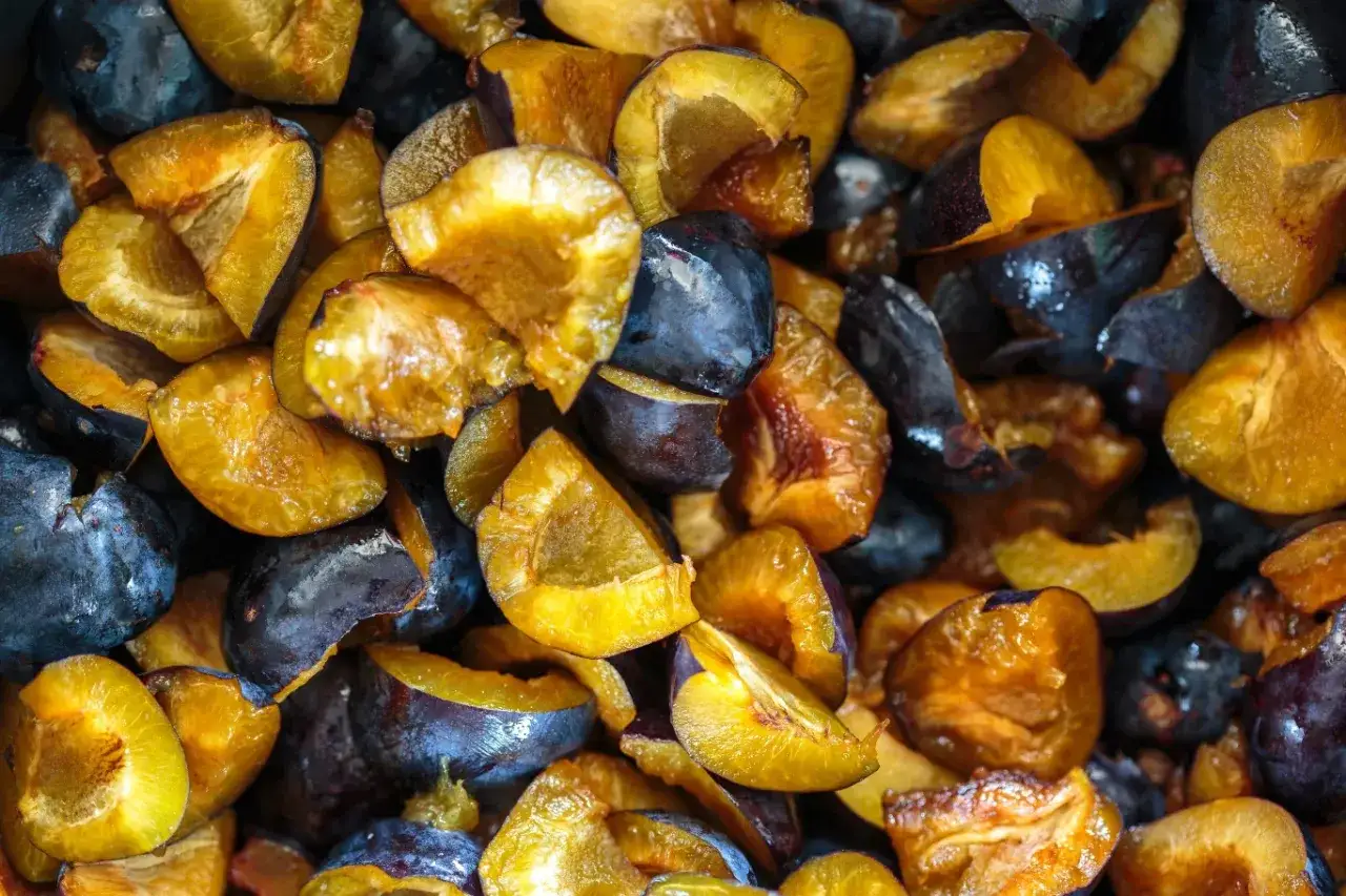 Pokrojone śliwki, zarówno całe, jak i połówki, ukazują swoje soczyste, żółte wnętrza i ciemnofioletową skórkę. Warto wiedzieć, że śliwki mają niski indeks glikemiczny, co czyni je zdrowym wyborem.