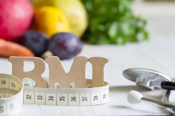 Litery "BMI" owinięte miarką, obok stetoskop i owoce. Zdjęcie sugeruje, czym obniżyć ciśnienie bez leków: zdrową dietą i kontrolą wagi.